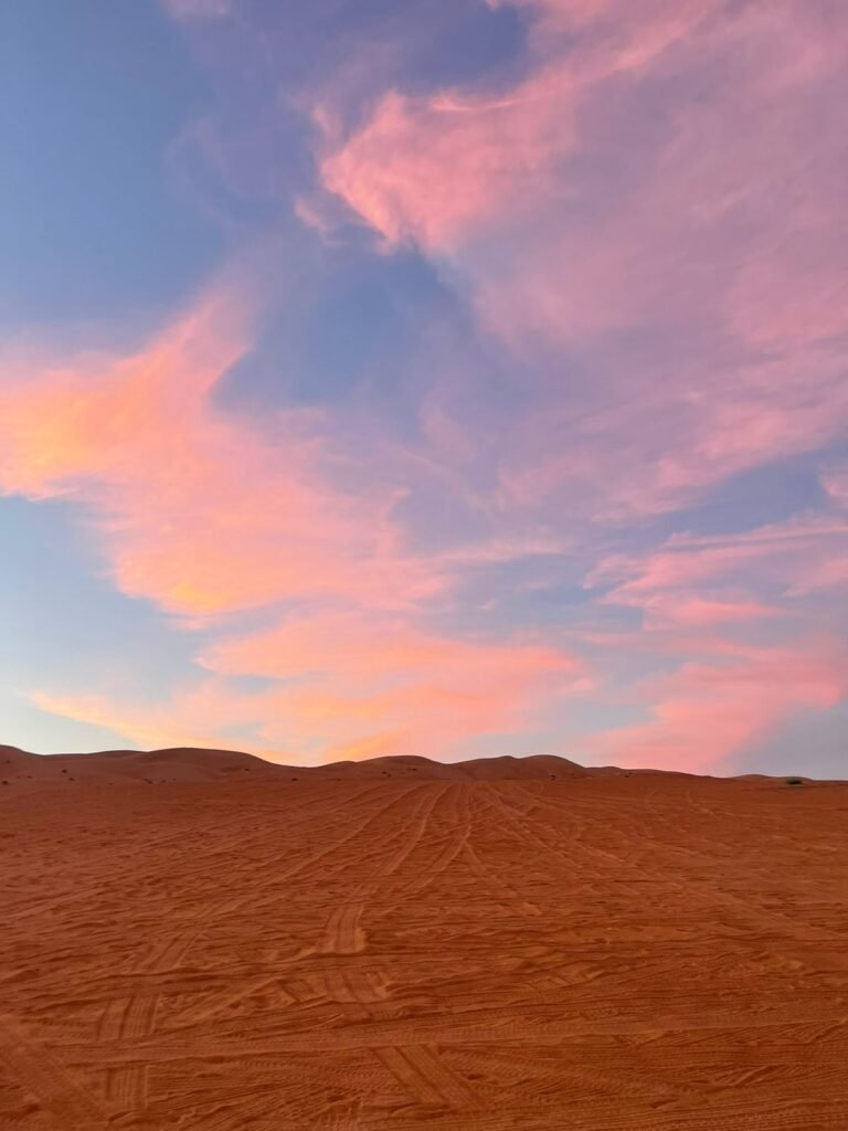Beautiful pink and orange sunset clouds stretching over the red desert sand dunes of Wahiba Sands in Oman.