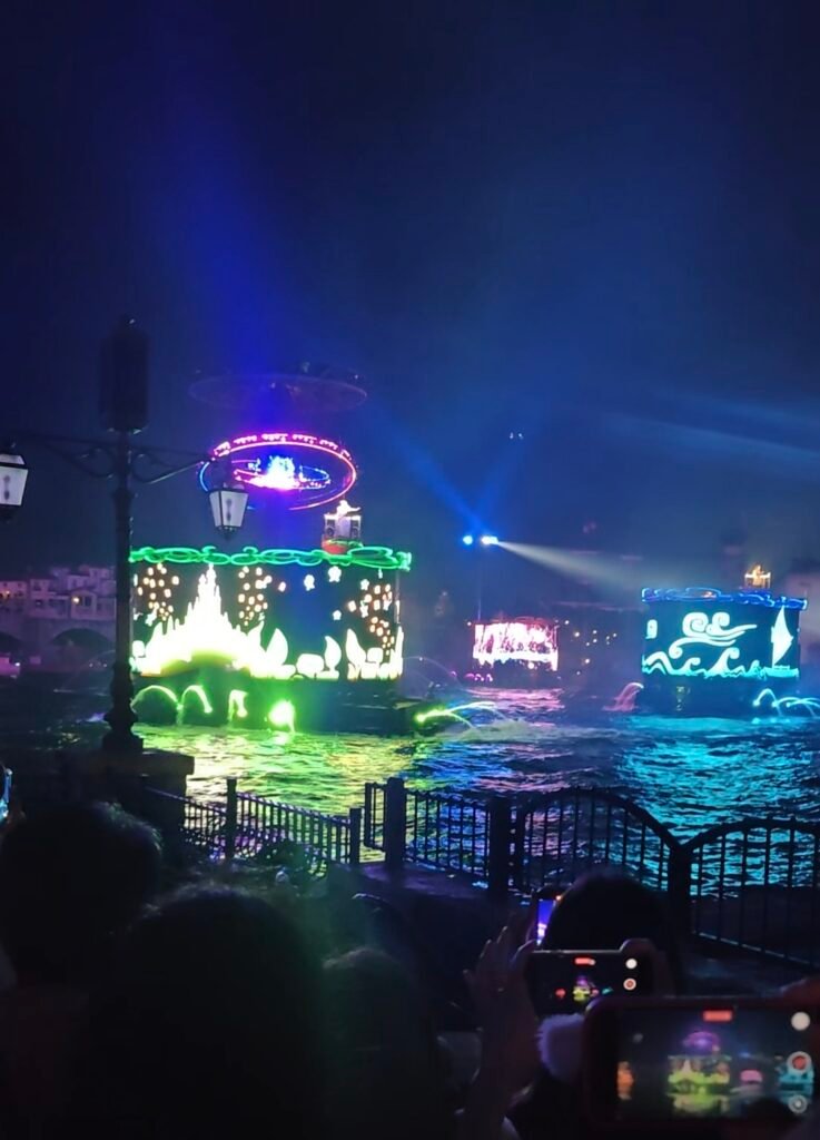 Illuminated water barges and colorful projection floats performing during a nighttime show at Tokyo DisneySea.