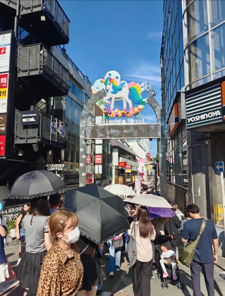 Crowds walking under the bright entrance archway of Takeshita Street decorated with a colorful unicorn motif in Harajuku.`