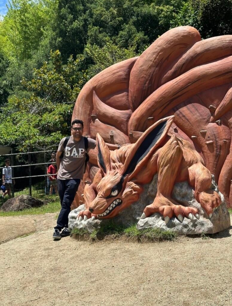 A VISITOR POSING NEXT TO A LARGE KURAMA NINE TAILED FOX STATUE AT NIJIGEN NO MORI