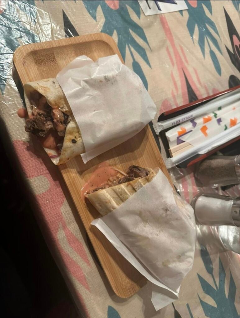 Two freshly wrapped grilled shawarma rolls with sliced meat and savory sauce served on a bamboo wooden board.