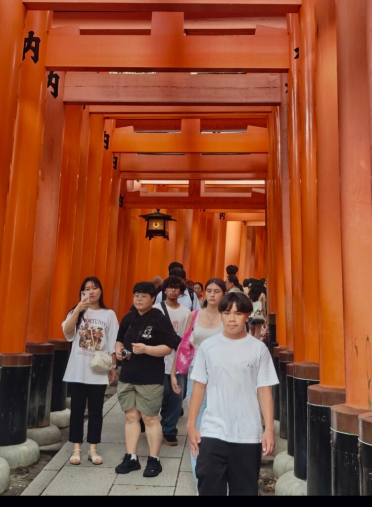 A scenic pathway framed by tightly aligned, vibrant vermilion-orange wooden torii gates at Fushimi Inari Shrine in Kyoto, Japan, featuring black base accents into the posts.