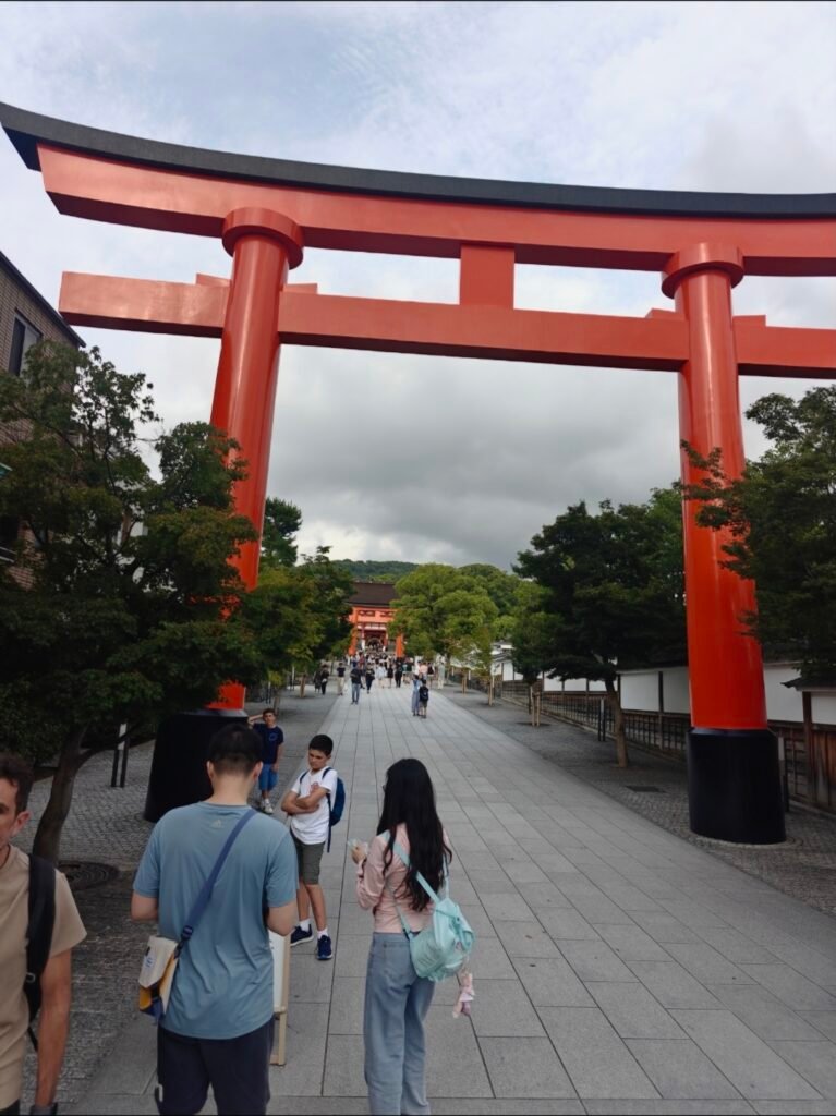 A MASSIVE BRIGHT ORANGE TORI GATE STANDING AT THE MAIN ENTRANCE PATH L;EADING TO FUSHIMA INARI SHRINE IN KYOTO