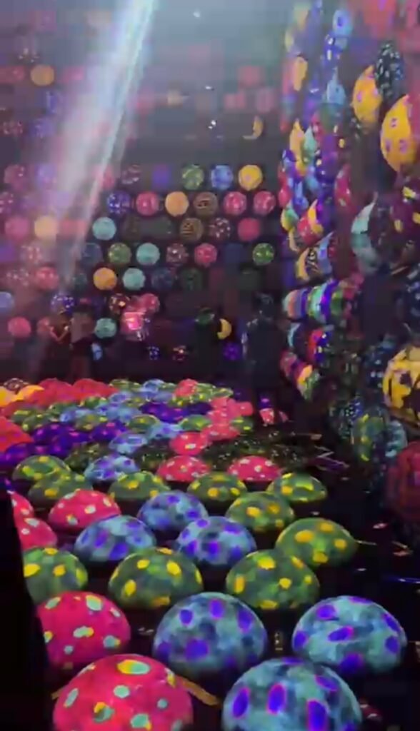 Vibrant, colorful illuminated dots and mushroom-like light installations reflecting inside an immersive digital art museum.