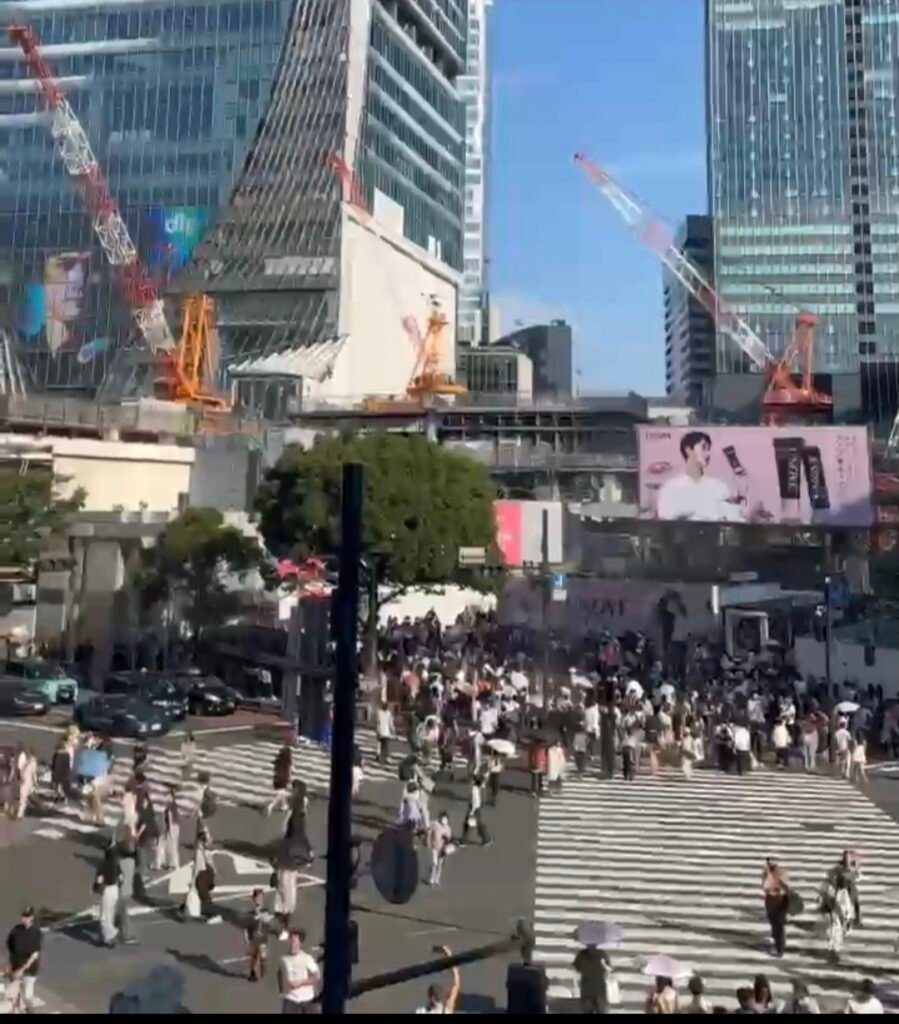 Elevated view of pedestrians crossing at Shibuya Crossing in Tokyo surrounded by skyscrapers and construction cranes.