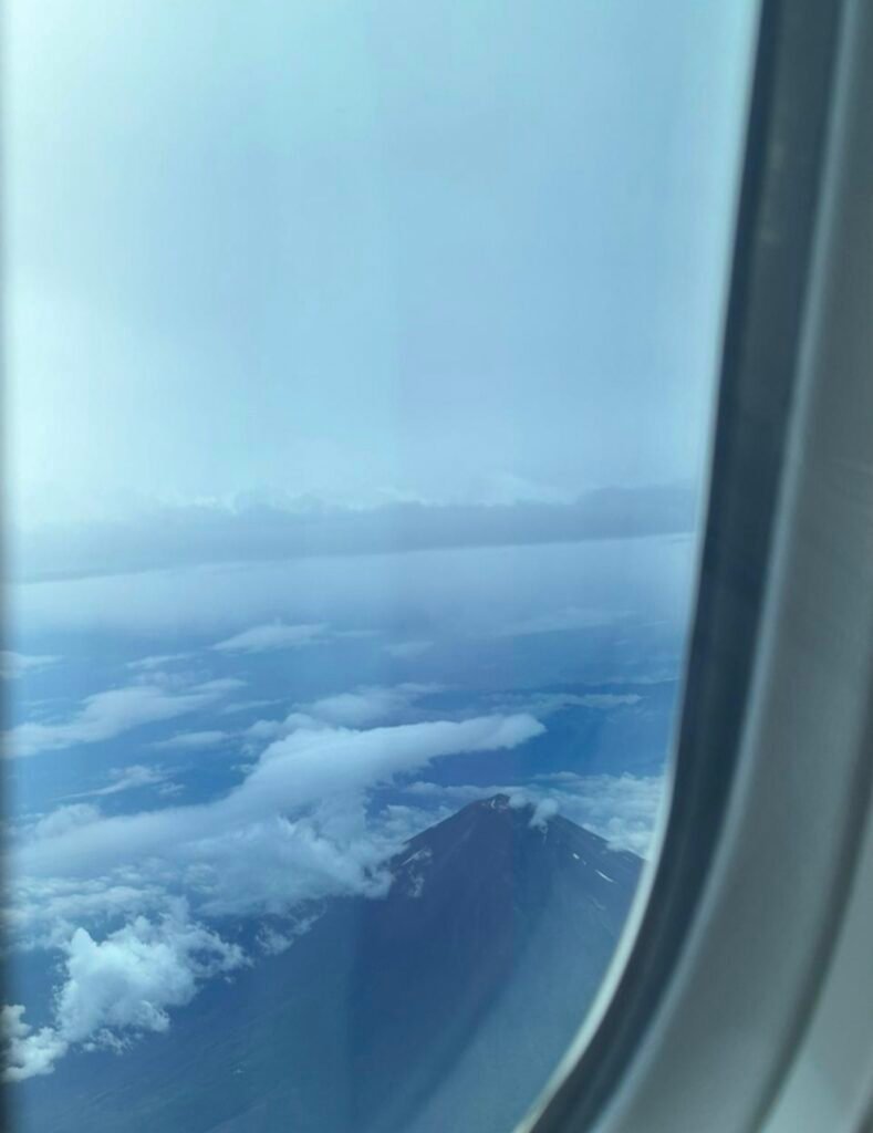 Aerial view of Mount Fuji's peak emerging through clouds taken from an airplane window.
