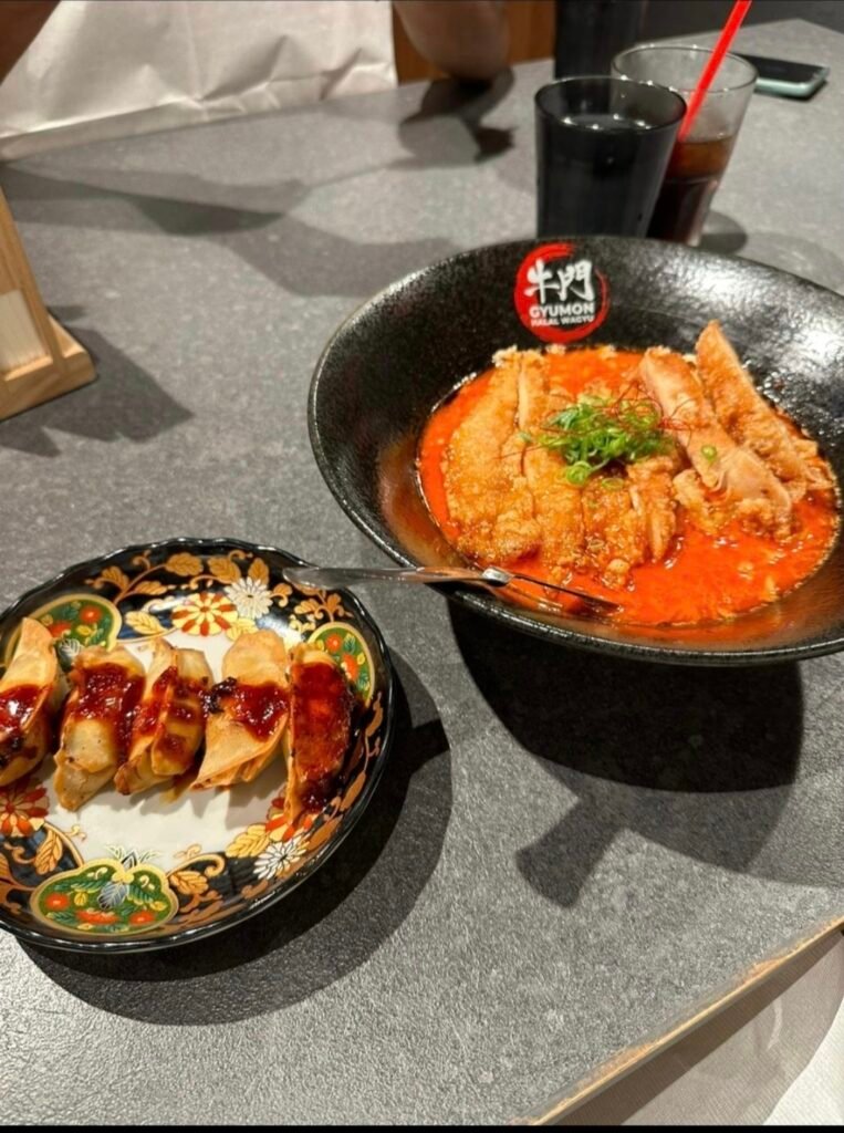 CRISPY FRIED CHOCKEN CUTLET RAMEN IN A SPICY RED BROTH ALONGSIDE A PLATE OF PAN FRIED GYOZA DUMPLING AT GYMON HALAL WAGYU IN SHIBUYA TOKYO 