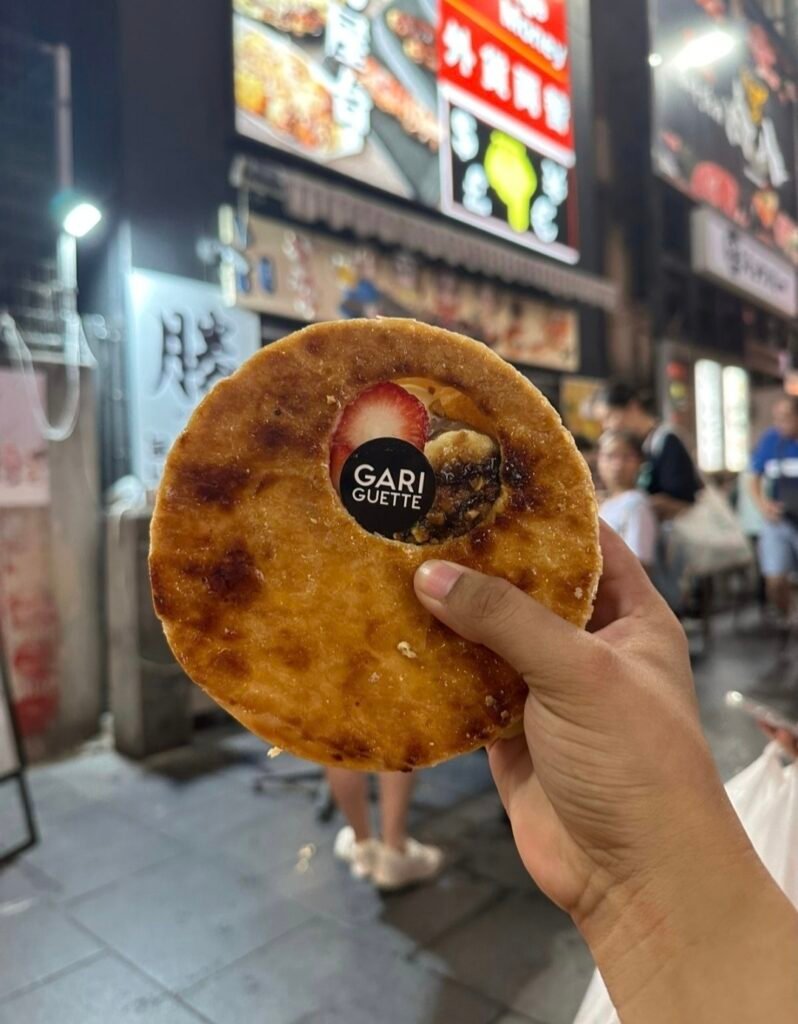 A HAND HOLDING A ROUND GARIGUETTE CARAMELIZED MILLE- PRESSE PASTRY FILLED WITH FRESH STRAWBERRY AND CUSTARD FILLING 