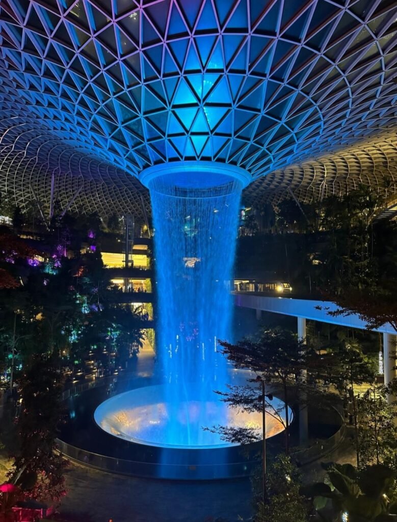 Spectacular indoor HSBC Rain Vortex waterfall illuminated with glowing blue lights at Jewel Changi Airport