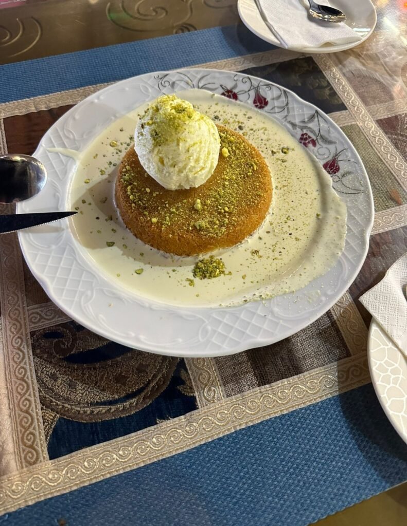  Warm Turkish Kunafa dessert topped with vanilla ice cream and crushed pistachios served on a sweet cream base.
