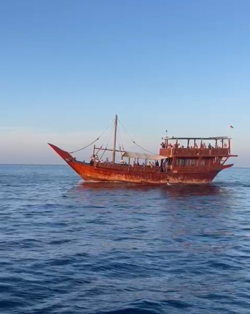 A traditional wooden Omani dhow cruise boat sailing across the blue ocean waters in Muscat, Oman.
